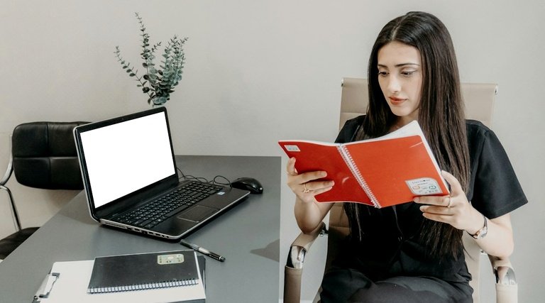 Mulher consulta caderneta vermelha ao lado de notebook para verificar direitos do 13º salário-maternidade